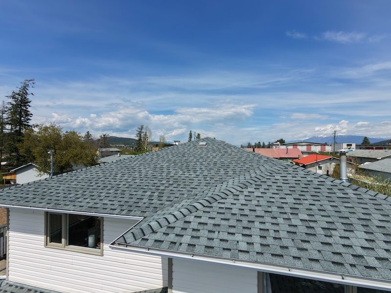 Wide-angle drone shot of large grey shingle roof with Kootenay mountains in background