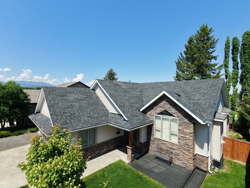 Drone view of stone-accented Cranbrook home with dark grey shingle roof after NuRoof treatment