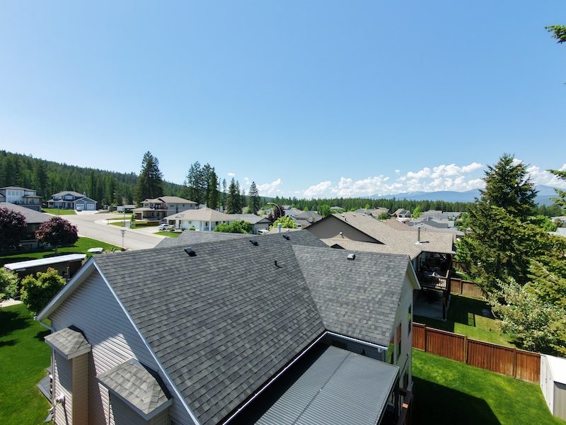 Neighbourhood aerial drone shot of grey shingle roof with Kootenay mountains and forest in background