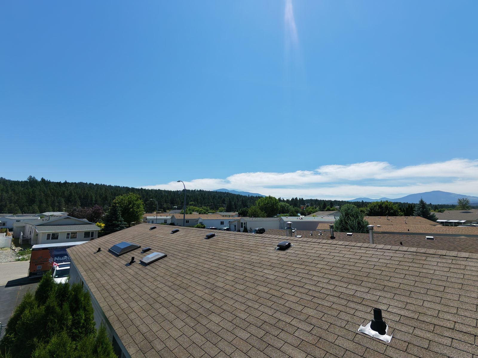 Aerial view of a tan shingle roof with skylights treated with NuRoof, mountain views in the background