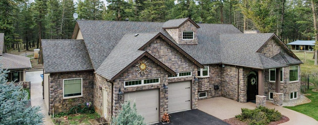 Exterior drone shot of a house with a double garage and stonework, and a grey asphalt shingle roof.